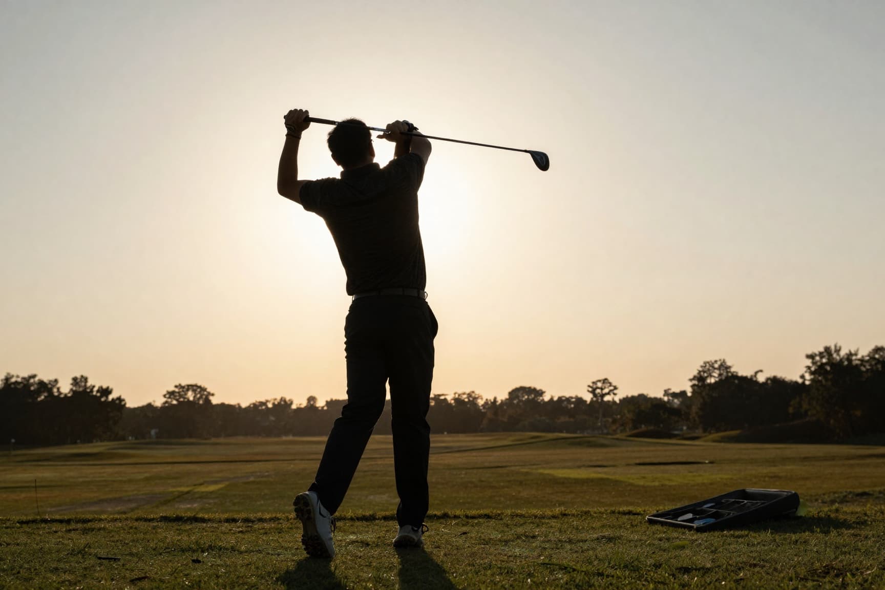 Golfer mid-follow-through on outdoor range at golden hour, Virginia mountains in distance